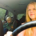 a mother driving the car with her kid in the backseat sitting in a car seat booster