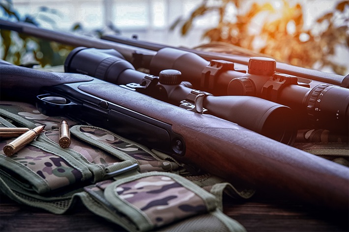 "A close-up view of two rifles with scopes placed on a camouflage-patterned mat, with bullets neatly arranged nearby.